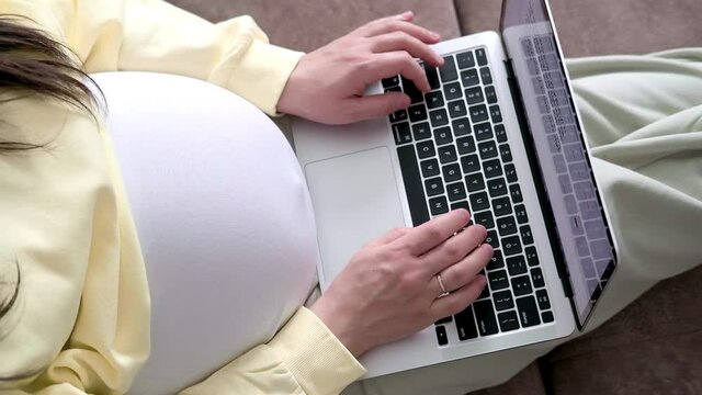 4k Top view Expectant mother working remotely online from home. Close up pregnant young woman hands on laptop with big belly advanced pregnancy