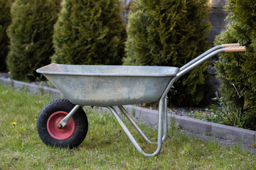 An empty dirty garden wheelbarrow stands on the green grass. Gardening and farming concept