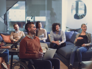 Disabled businessman in a wheelchair at work in modern open space coworking office with team