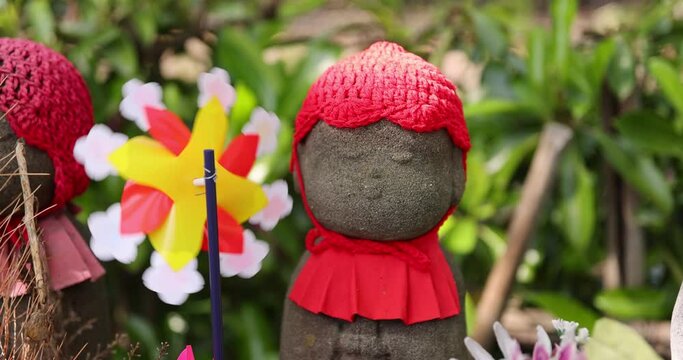 A slow motion of moving colorful windmills with Jizo statue daytime closeup