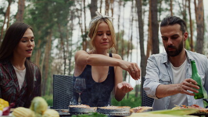Smiling girl finishing cooking food outside. Woman adding spices on fish