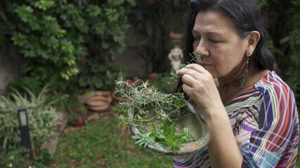Adult woman smelling collected herbs in wooden bowl