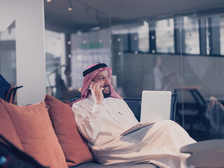 Mobile business communication and entrepreneurship. Arab businessman talking on smartphone and using laptop computer at workplace at home office