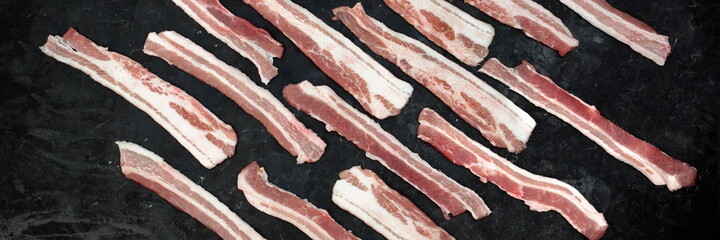 Cold Sliced Bacon On Black Table Grunge Background, Overhead View. Streaky Fresh Bacon Top View.