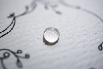 Detalle de gota de agua sobre papel con textura blanco y dibujo atrás desenfocado