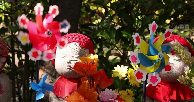 A slow motion of moving colorful windmills with Jizo statue daytime closeup