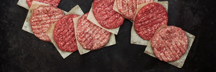 Raw Beef Hamburger Patties On Paper And Black Background, Overhead View. Raw Burger Cutlets On Isolated Background, Top View. Many Raw Minced Steak Burgers from Beef Pork Meat on Black Background.