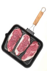 Striploin Beef Steaks on Grill Pan Isolated On White Background. Cast Iron Grill Pan with Raw Sirloin Beef or Veal Steaks White Isolated, Top View. Three Sirloin Beefsteaks, Overhead View.