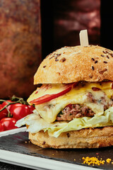 Big burger with juicy cutlet, cheese, tomato, lettuce on a black plate on the background of copper plates.