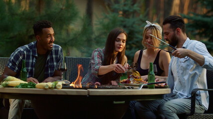 Young people putting grilled meal on plate. Happy fellows cooking bbq food