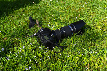 Photo camera with telephoto lens in grass.