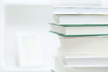 Book stack on white desk and light blurred bookshelf and photo frame in the living room. Education background. Reading, relaxing. Lifestyle.