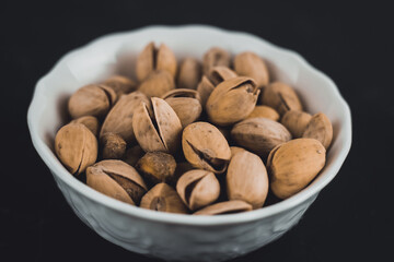 Pistachios in a white plate on a dark background