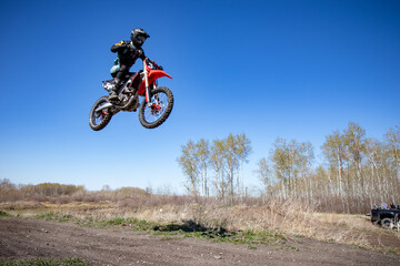 Man in black riding gear soaring through the air on a dirt bike.