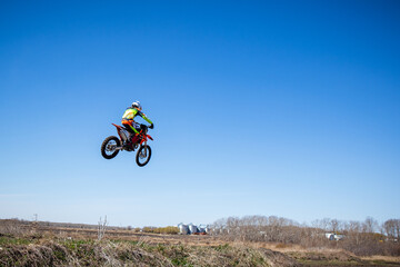 Naklejka na ściany i meble Man on dirt biker soars through the sky as they race around a track.