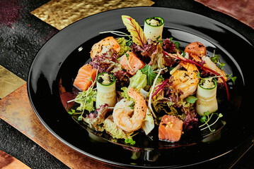 Salad with salmon, shrimps, lettuce, cucumber and soybean sprouts in a black plate on a background of copper plates