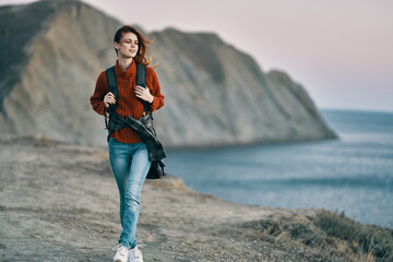 woman tourist with a backpack on her back walks on the beach near the sea in the mountains