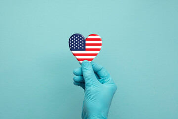 Hands wearing protective surgical gloves holding USA flag heart