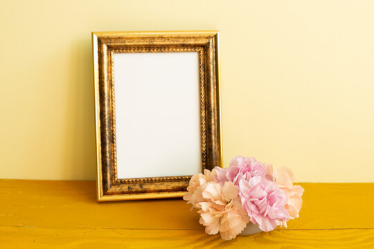 Empty photo frame with carnation flowers on wooden table. yellow background