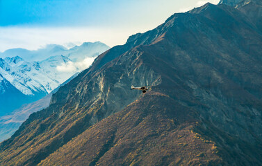 a small plane flying along the mountains of Alaska dwarfed by the size of the mountain.
