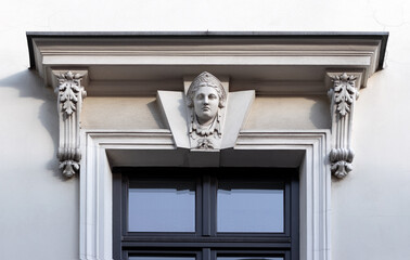 Dekoracyjny detal architektoniczny. Klasyczna rzeźba głowy na zwieńczeniu okna.  Rzeżba na obramieniu okna.  Fasada kamienicy w Starym Mieście. Europa
