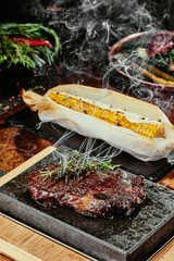 Fermented steak. Steak with rosemary on a black plate served with grilled corn on a background of greens, spices and fresh vegetables, on a copper sheet