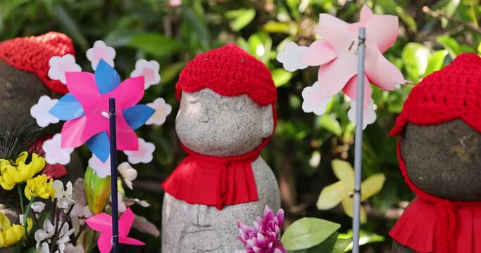 A slow motion of moving colorful windmills with Jizo statue daytime closeup