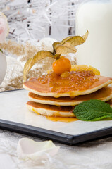 Pancakes with physalis jam, decorated with physalis berry on a white plate on a light spring background. Healthy breakfast. 