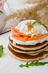 Pancakes with salmon, poached egg and arugula on white plate on a light background. Healthy breakfast. 