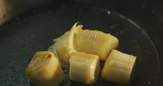 The cook adds a tablespoon of butter to the fried banana slices in a hot skillet
