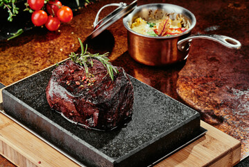Grill steak. Fillet of Mignon on a black plate on a background of greens, spices and vegetables, on a copper sheet