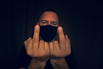 White Latin man with black mask and black T-shirt looking at the camera making a blunt signal to the camera.