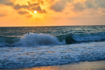 Ocean waves crashing onto the shore during a beautiful orange sunset