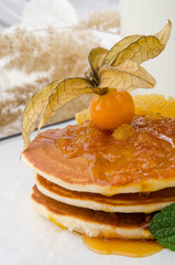 Pancakes with physalis jam, decorated with physalis berry on a white plate on a light spring background. Healthy breakfast. 