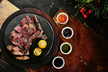 Fermented steak. T-Bone Steak with grilled vegetables on a black round plate on a background on a...