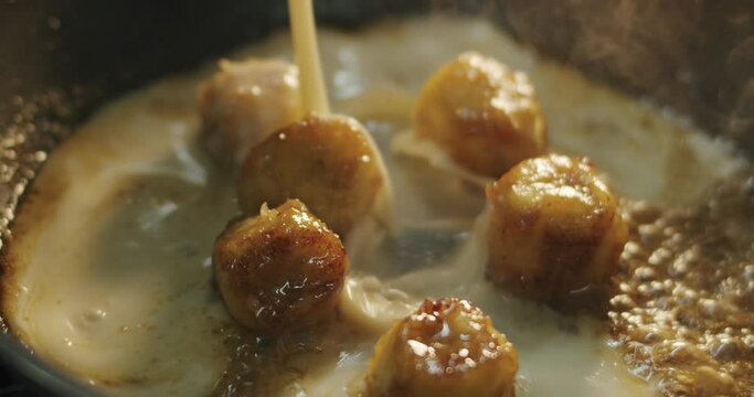 The cook adds cream to the fried banana slices in a hot skillet