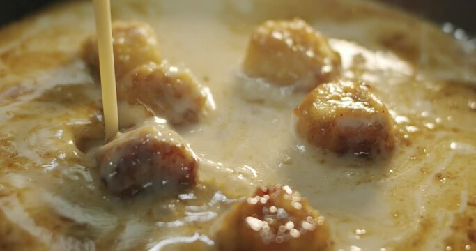 The cook in a thin stream adds coconut milk to hot fried bananas in a hot skillet and stirring it