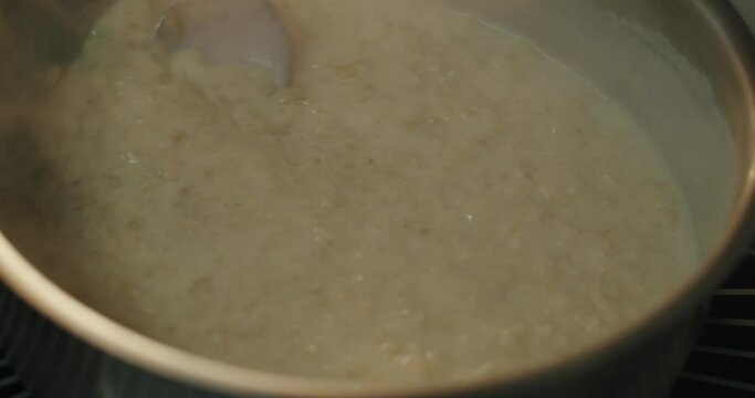 Chef's hand stirring boiling oatmeal milk porridge with a tablespoon in slow motion