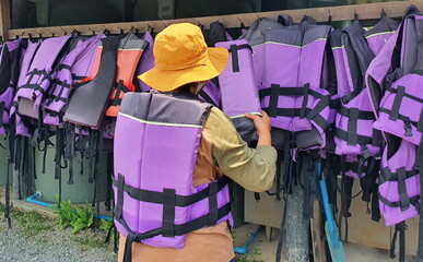 Tourists in yellow hats are choosing the right size purple life jacket to wear before heading out for water activities.Should wear a life jacket every time you play in the water for safety in accident