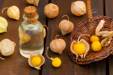 Cape Gooseberry (Physalis Peruviana) fruits essence oil in a glass bottle with cork. Also there are fruits with capsules over a wooden brown table and other are in a basket.