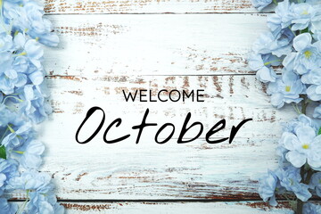 Welcome October text and blue flower decoration on wooden background
