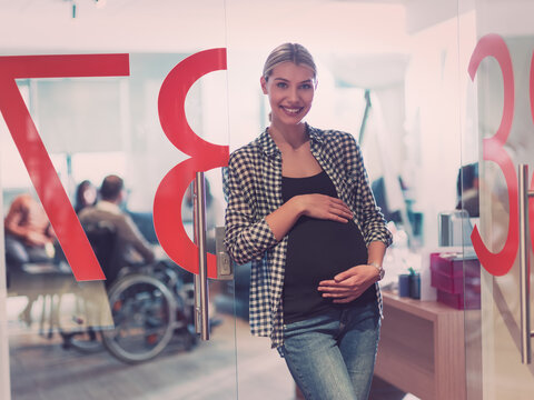 Portrait of pregnant businesswoman gently holding belly in modern office