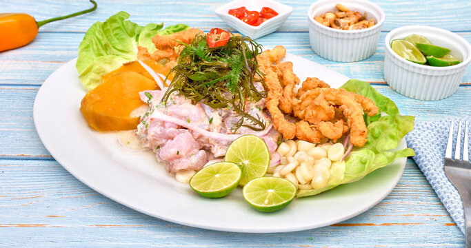 Peruvian food: fish ceviche and chicharron de pescado with fried cassava, sweet corn and sweet potato, served on a white plate