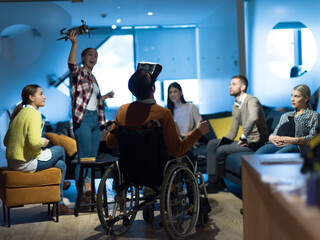 Disabled businessman in a wheelchair at work in modern open space coworking office with team using...