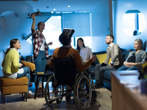 Disabled businessman in a wheelchair at work in modern open space coworking office with team using virtual reality googles drone assistance simulation