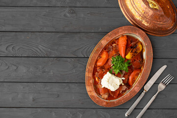 Steamed meat with vegetables in tomato sauce on wooden background