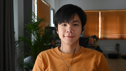 Head shot of young man wearing head phone while sitting in home office. - obrazy, fototapety, plakaty