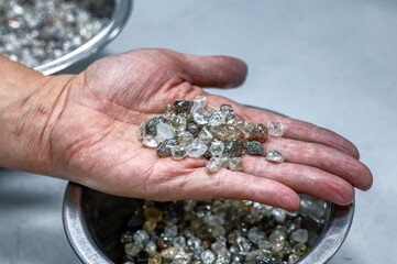 A wide variety of rough diamonds are in the palm of your hand. Many small gems