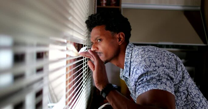 African man looking through window blinds