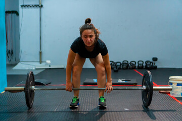 latina sportswoman lifting a barbell with weight on a disc, inside the gymnasium
